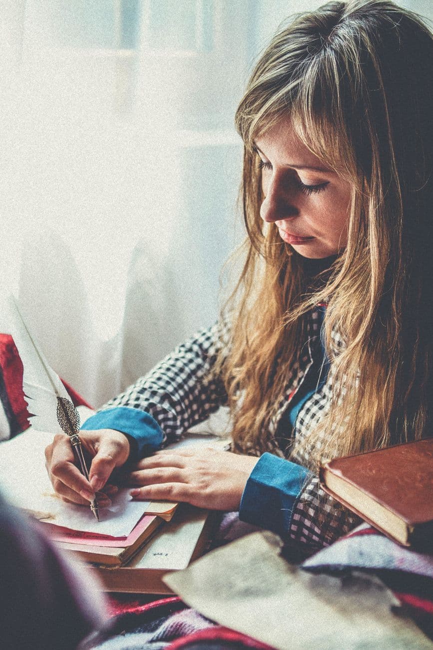 A person writing in a journal by a window
